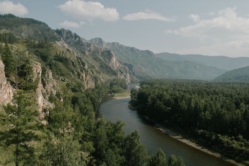 Free Narrow rippled river between rough mount and lush trees under misty sky in daytime Stock Photo