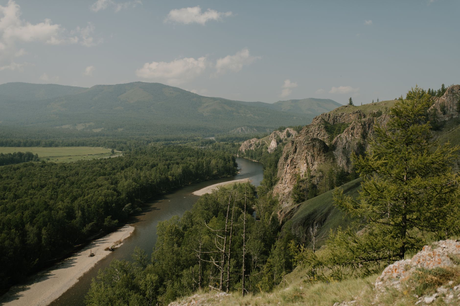Scenic view of narrow river between green trees and rough ridges under cloudy sky on misty day