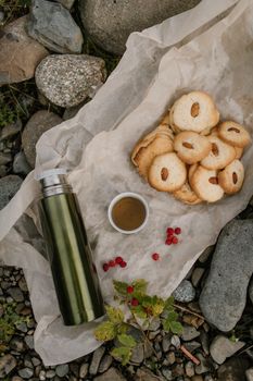 户外野餐场景舒适宜人，配有杏仁饼干、保温瓶和羊皮纸上的一杯茶
