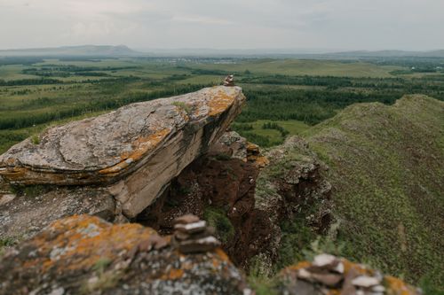 Free Drone view of stony rough terrain with uneven surface near green meadows with herb and forests under cloudy sky Stock Photo