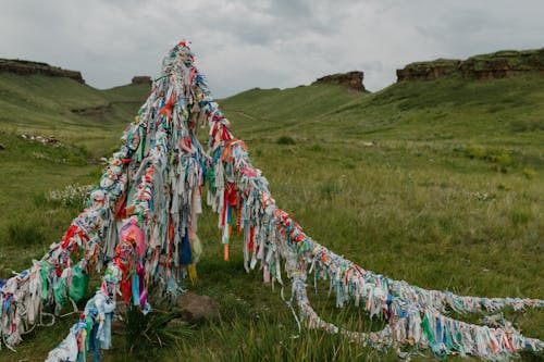 Tibetan bright flags located in field with fresh green grass and rocky formations under cloudy sky
