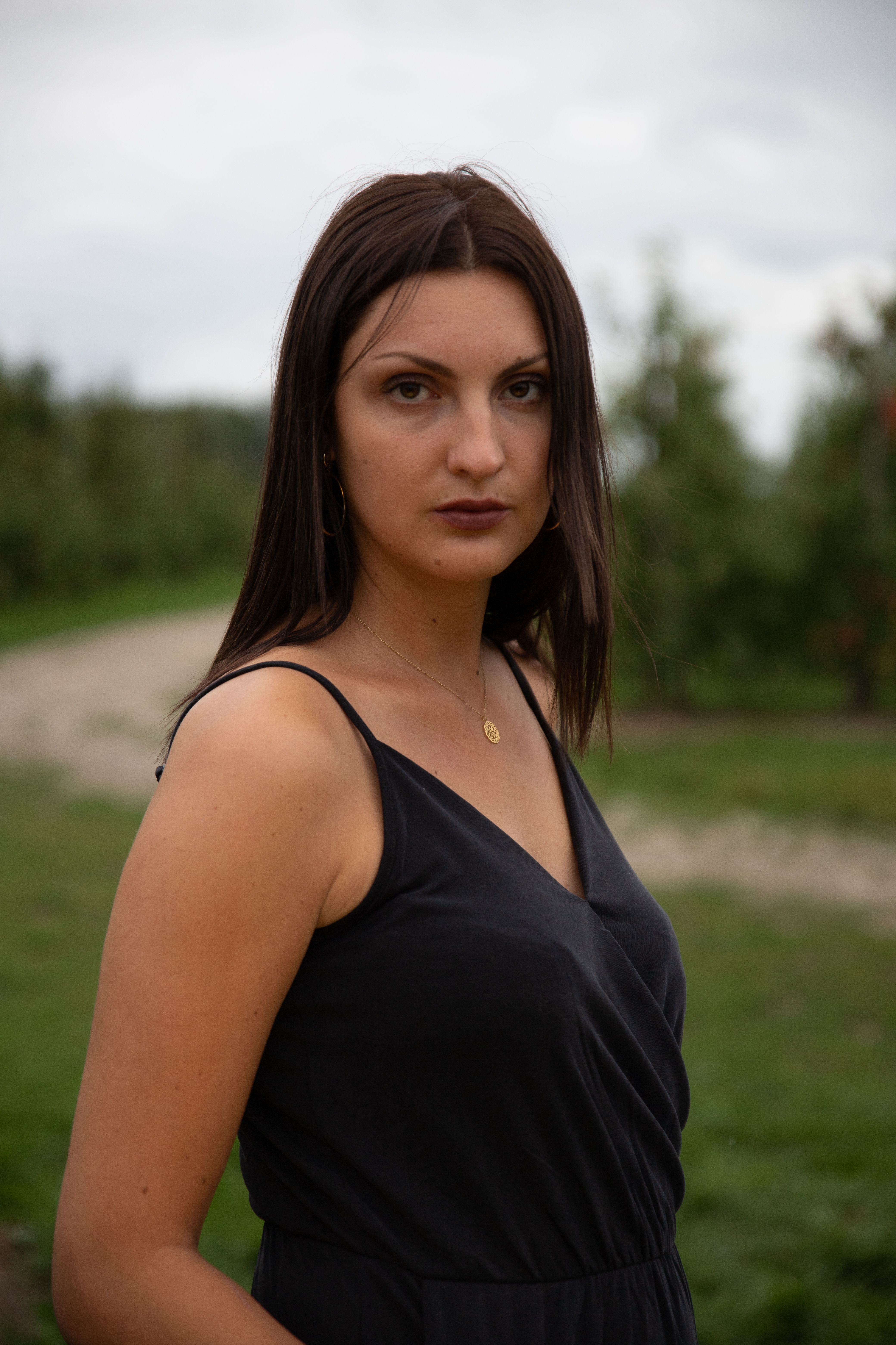 Portrait of a serious brunette woman in a black dress outdoors, showcasing a pensive look.