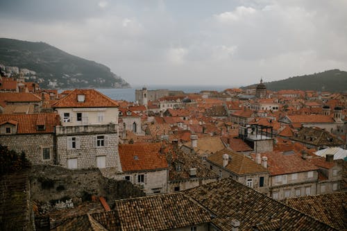 Cityscape of residential houses with tiled roofs and brick walls on hills near calm ocean in overcast weather