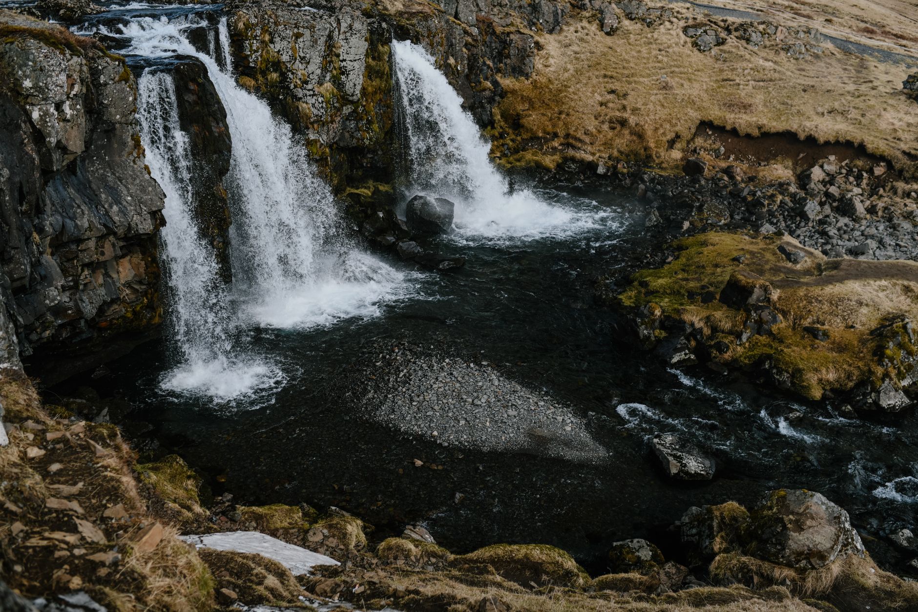Kvernufoss waterfall cascading down a green mossy cliff into a rocky gorge