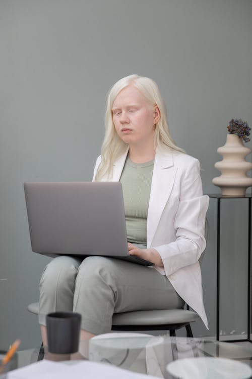 Serious young albino female manager in stylish formal outfit using laptop while sitting on chair in cozy office