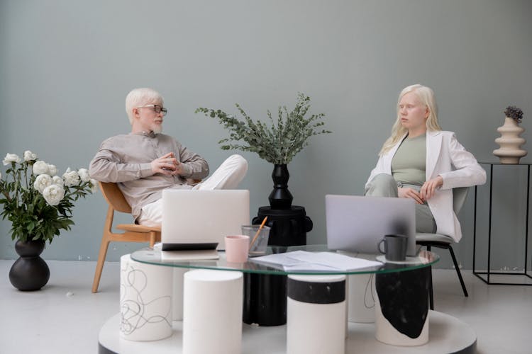 Serious Business Partners Discussing Project In Stylish Office Sitting At Table With Netbooks