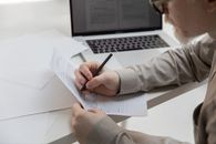 Crop office employee working with document near laptop