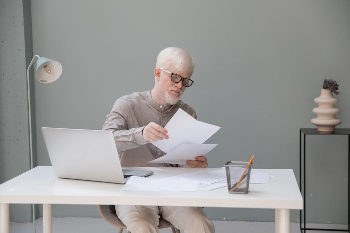Albino concentrated office worker in eyeglasses watching documents at desk with netbook in daylight