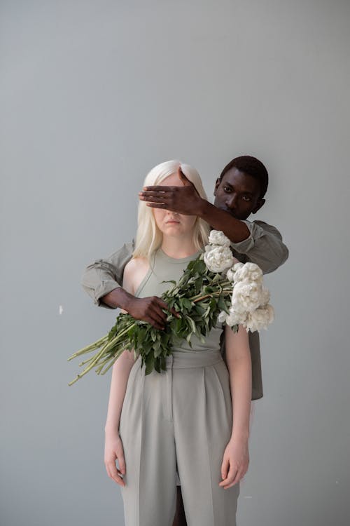 Black man with flowers covering eyes of unrecognizable female beloved