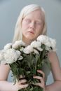 Relaxed female with blond hair and pale skin standing with closed eyes on gray background with bouquet of flowers in hands