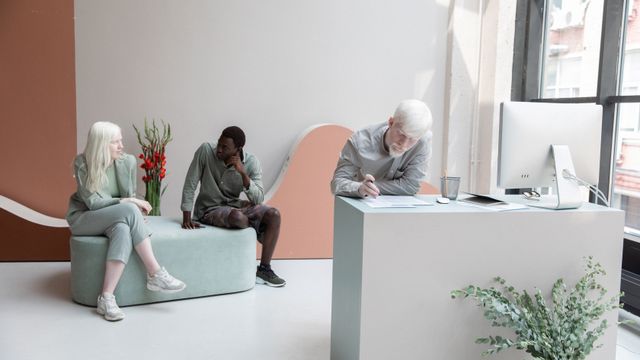 Full body of multiethnic coworkers sitting on sofa and writing on paper while working together in contemporary office with computer