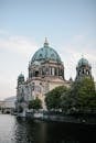 Exterior of impressive Berlin Cathedral with green sandstone dome built in Neo Renaissance style on rippling river coast under blue sky