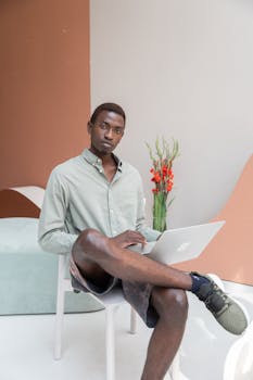 Confident young man in casual attire working on a laptop in a contemporary office setting.