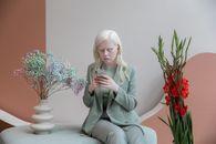 在现代花卉装饰的室内空间里，一位浅色头发的成年女性正专注于智能手机