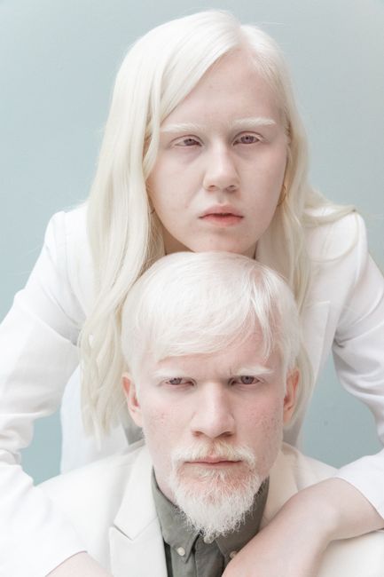 Portrait of charismatic couple in white clothes standing close against gray background and looking at camera