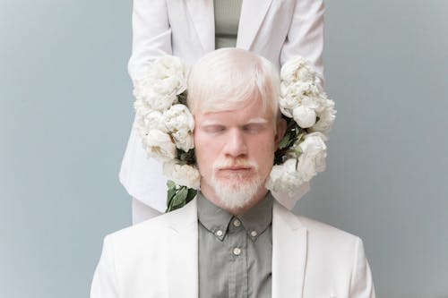 Crop woman holding flowers near head of calm male in formal suit against gray background
