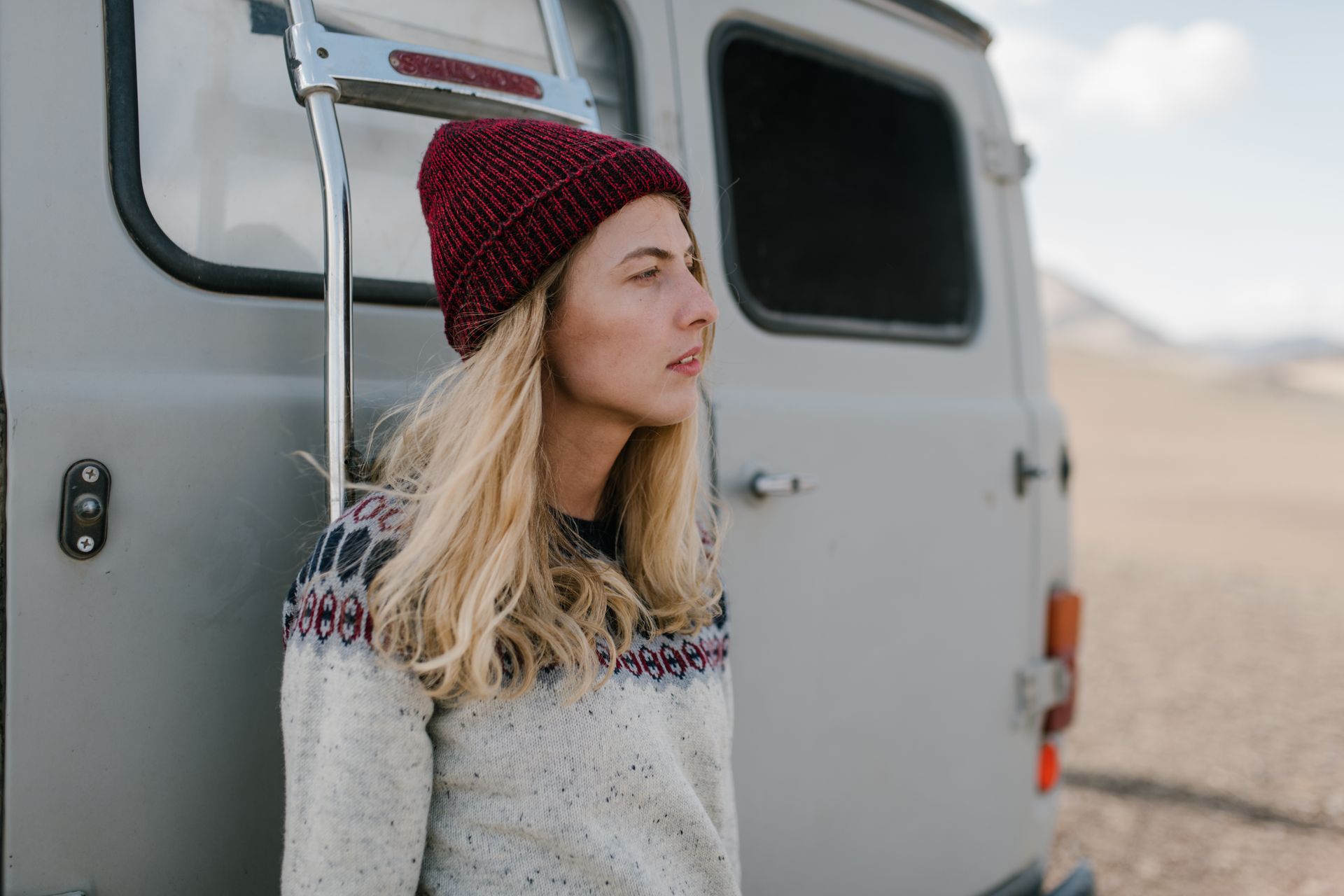 Young female in casual clothes and hat standing near van and looking away