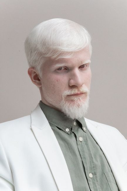 Low angle of handsome blond haired male with beard standing against gray background and looking at camera