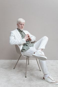 一位身穿白色西装的时尚男士，自信地坐在室内，散发着优雅与时尚的气息