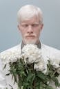 Albino male standing against gray background with closed eyes and holding bouquet of blooming flowers