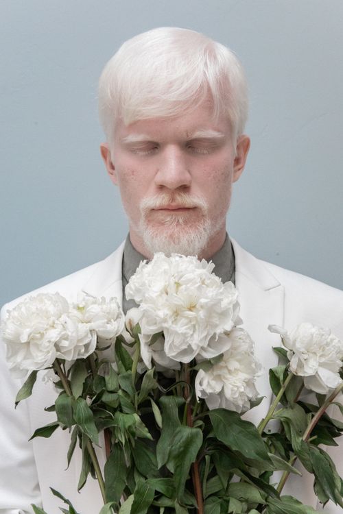 Free Albino male standing against gray background with closed eyes and holding bouquet of blooming flowers Stock Photo