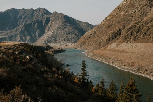 宽阔的河流在岩石山脉之间流淌，树木和草地点缀的山区地形风景如画