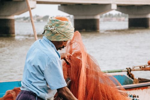 Free Fisherman arranging fishing nets on a boat near a bridge, outdoor setting. Stock Photo