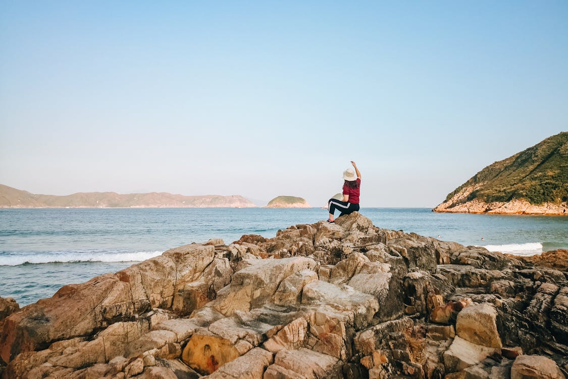 Woman sitting on rocky coast near waving sea