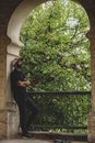 Man Leaning Under Arch and Green Tree in Background