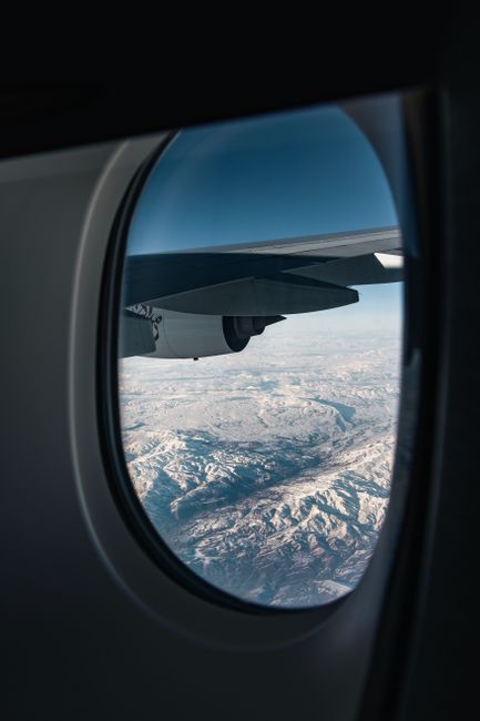 Aerial view of snow-covered mountains through an airplane window, capturing a serene travel moment.