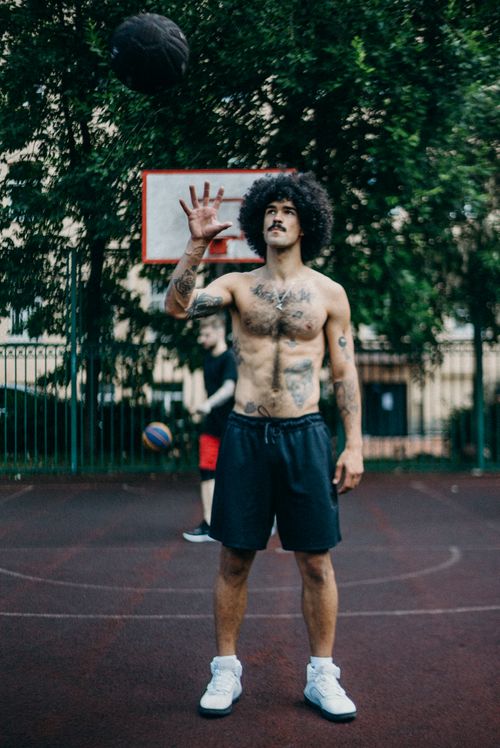 Free A shirtless athlete practicing basketball outdoors on a court with tattoos and afro hairstyle. Stock Photo