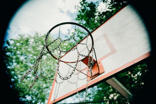 A basketball hoop with chain netting depicted from a low angle, against a clear sky.