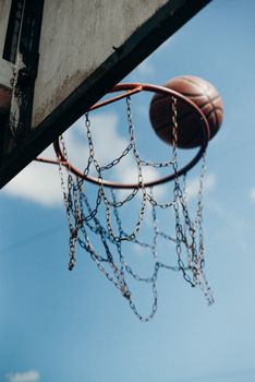 A dynamic photo capturing a basketball mid-air near a rustic hoop against a clear blue sky.