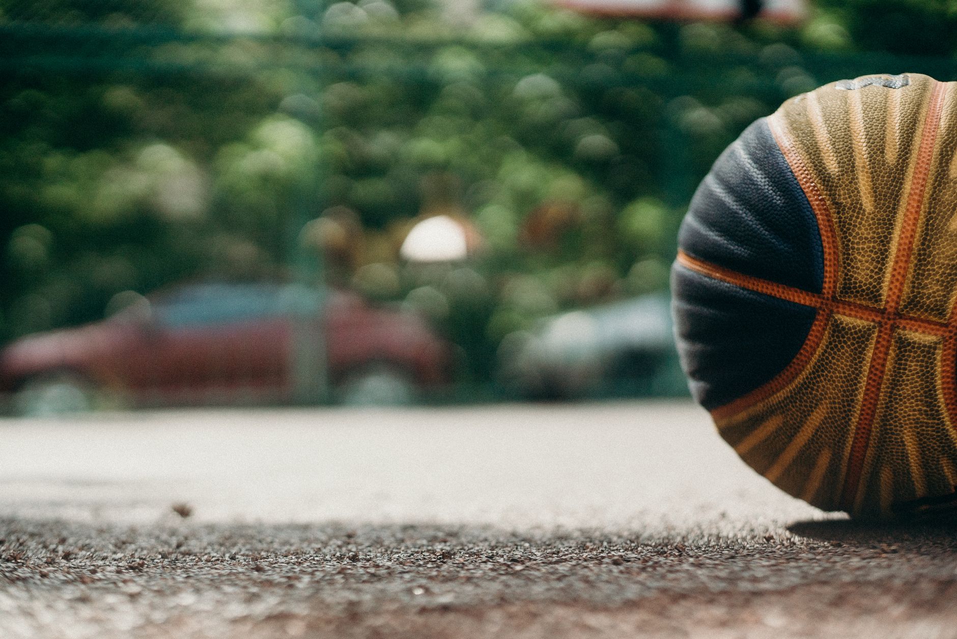 Detailed image of a basketball resting on an outdoor court surface with blurred car background.