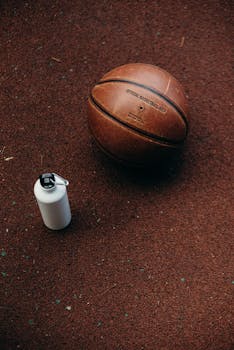 Close-up of a basketball and a water bottle on a textured court surface, ideal for sports content.