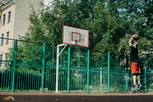 A man shooting a jump shot on an outdoor basketball court surrounded by trees.