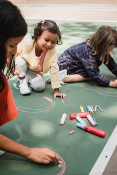 Three kids enjoy drawing with colorful chalk on a sunny day at the playground.