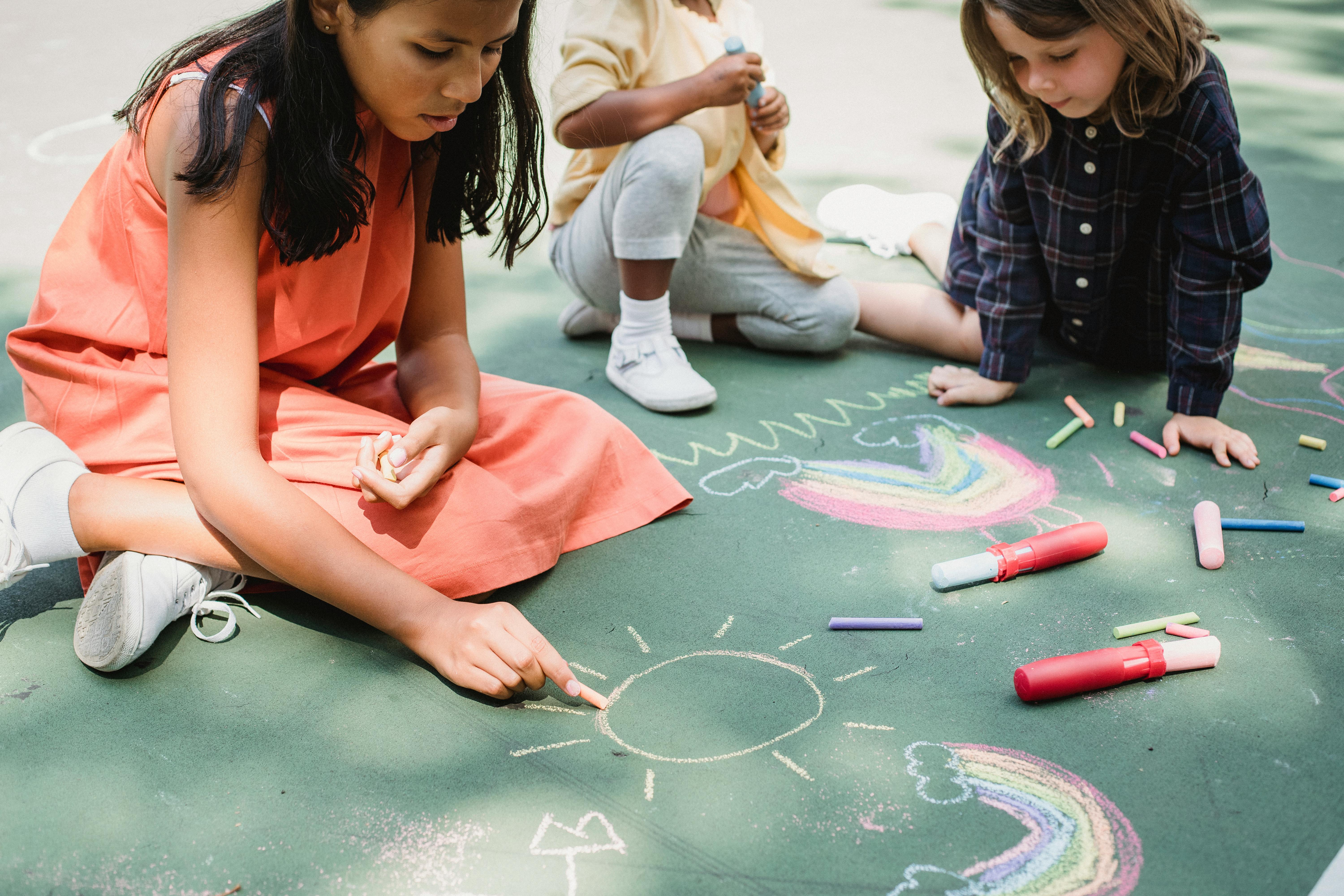 三个孩子在人行道上用彩色粉笔画着彩虹和阳光