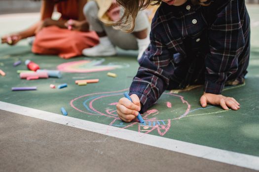 Kids enjoying creative drawing with colorful chalk outdoors on a playground.