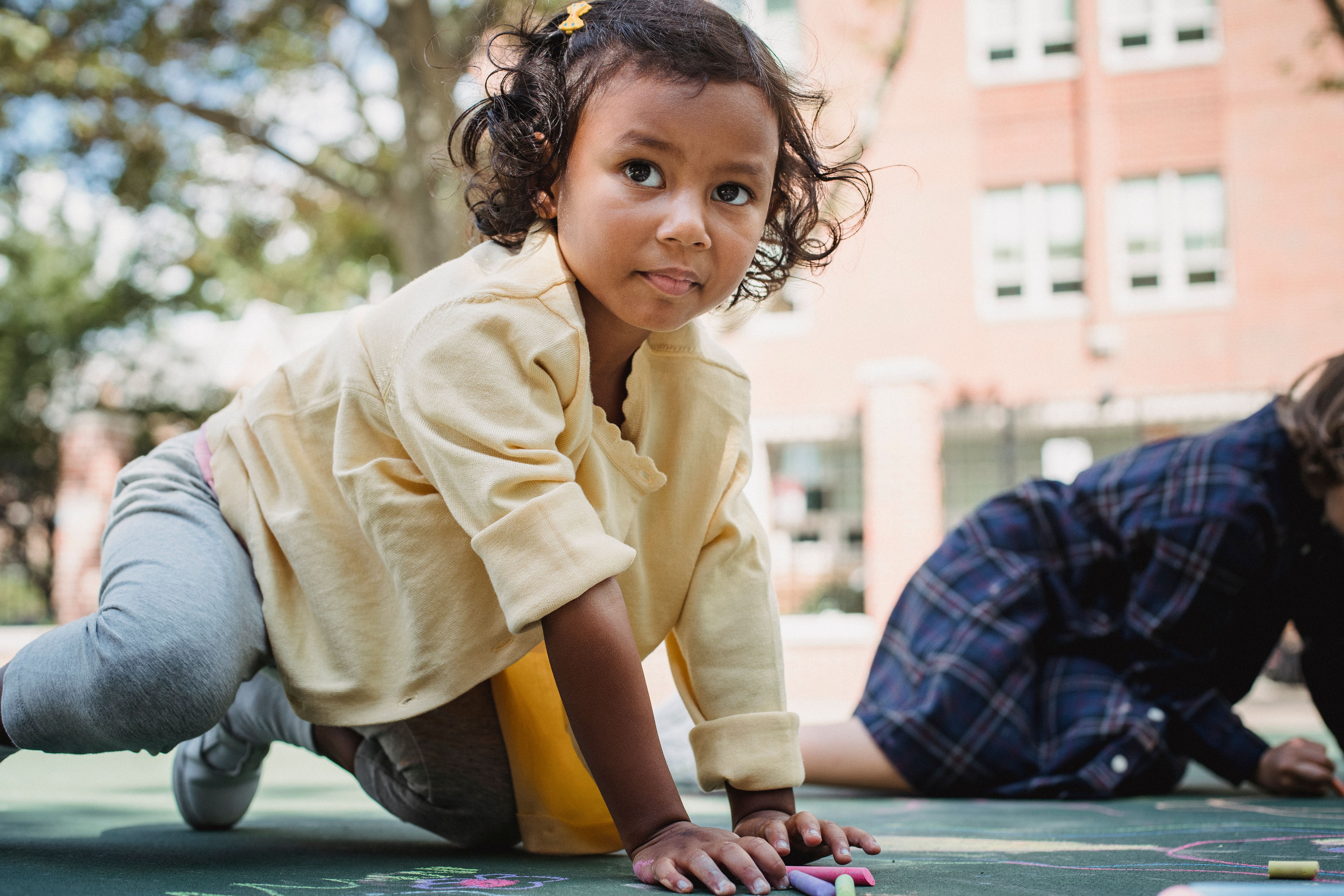 A young child playfully draws with chalk on an outdoor pavement at a playground.