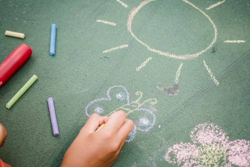 Free A child draws a sun and butterfly on pavement with colorful chalk sticks outdoors. Stock Photo