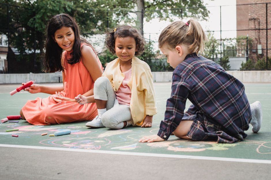 Three children drawing with chalk on a sunny outdoor court. Fun and creativity in action.
