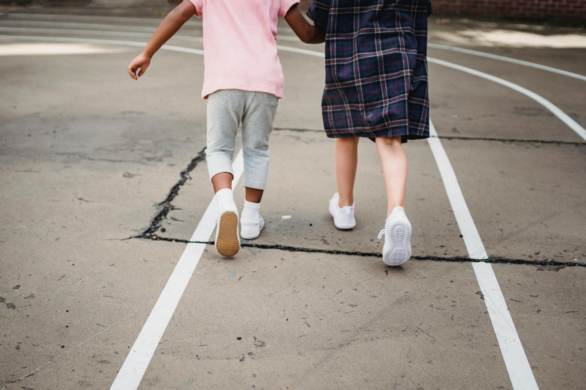 Rear view of children walking together on a school playground with white line markings.