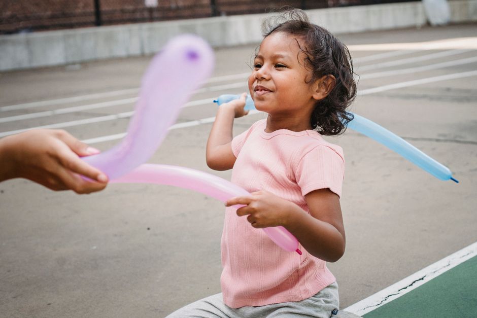 Smiling child playing with colorful balloons outdoors in a playground.