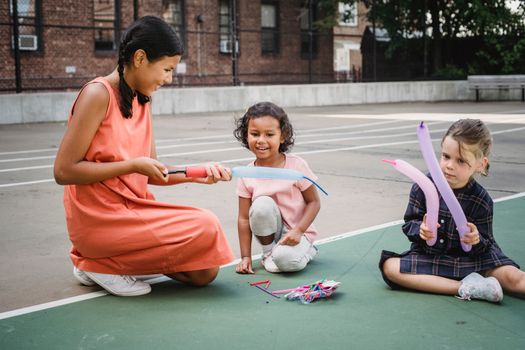 Three children enjoying a playful balloon activity outdoors on a concrete court.