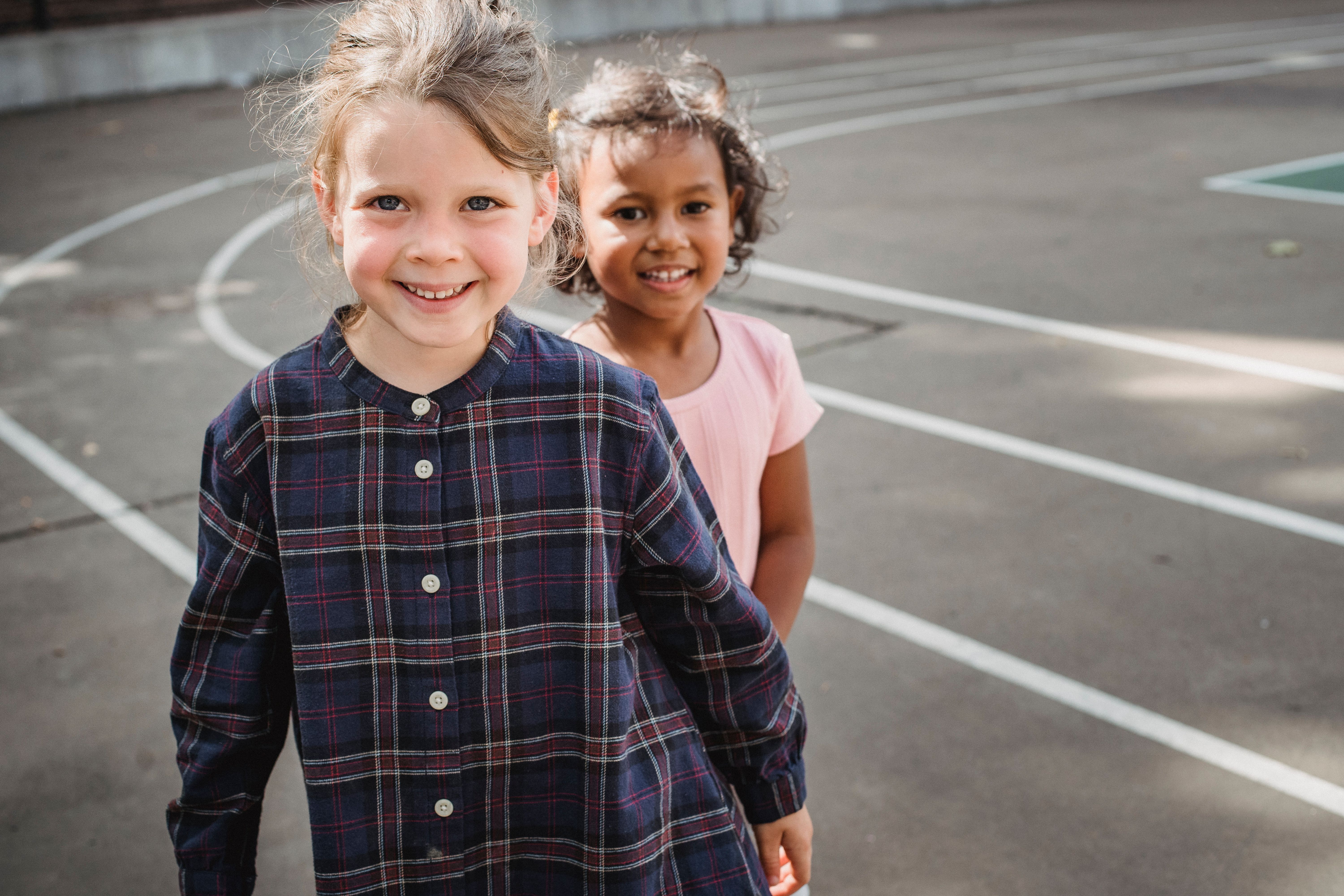 Two young girls smiling happily while playing outdoors on a sunny day.