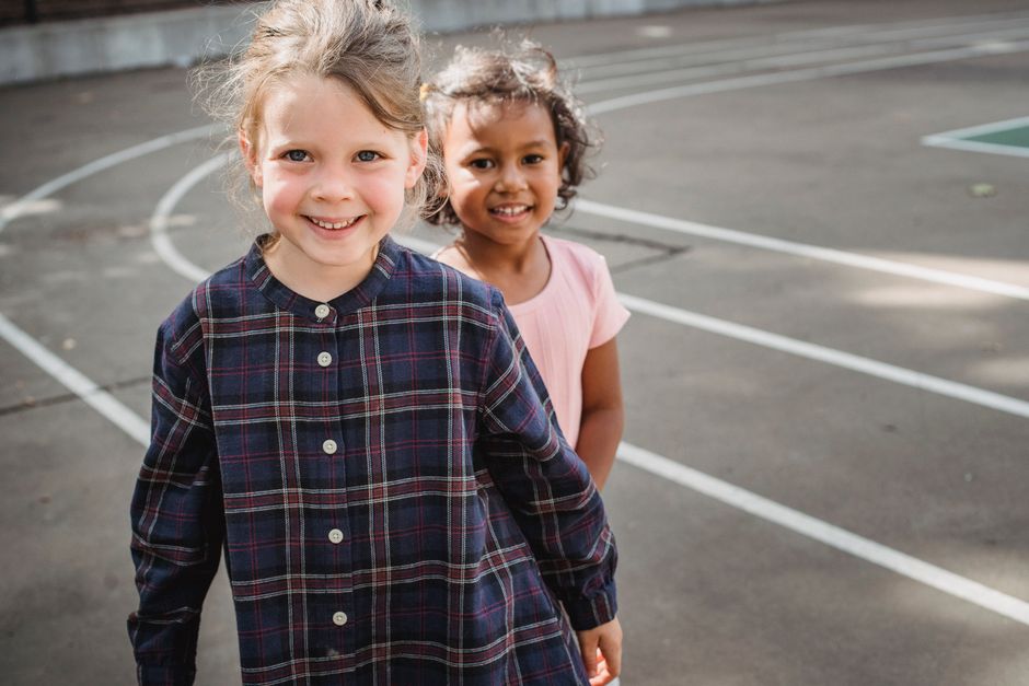 Two young girls smiling happily while playing outdoors on a sunny day.