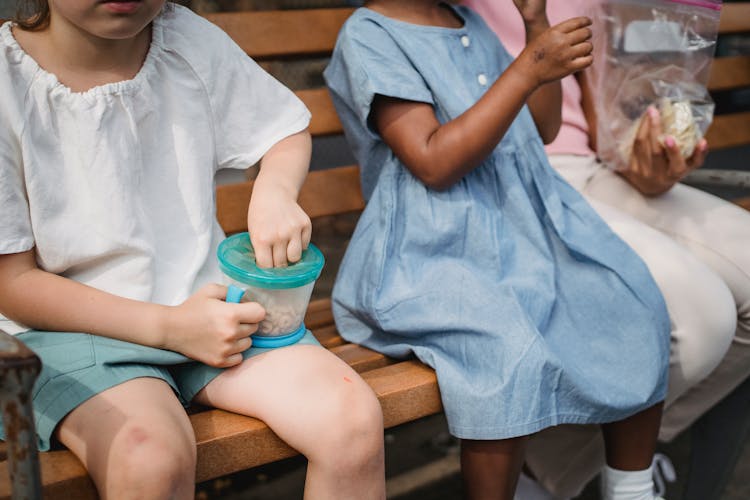 Children Eating Snacks On A Wooden  Bench