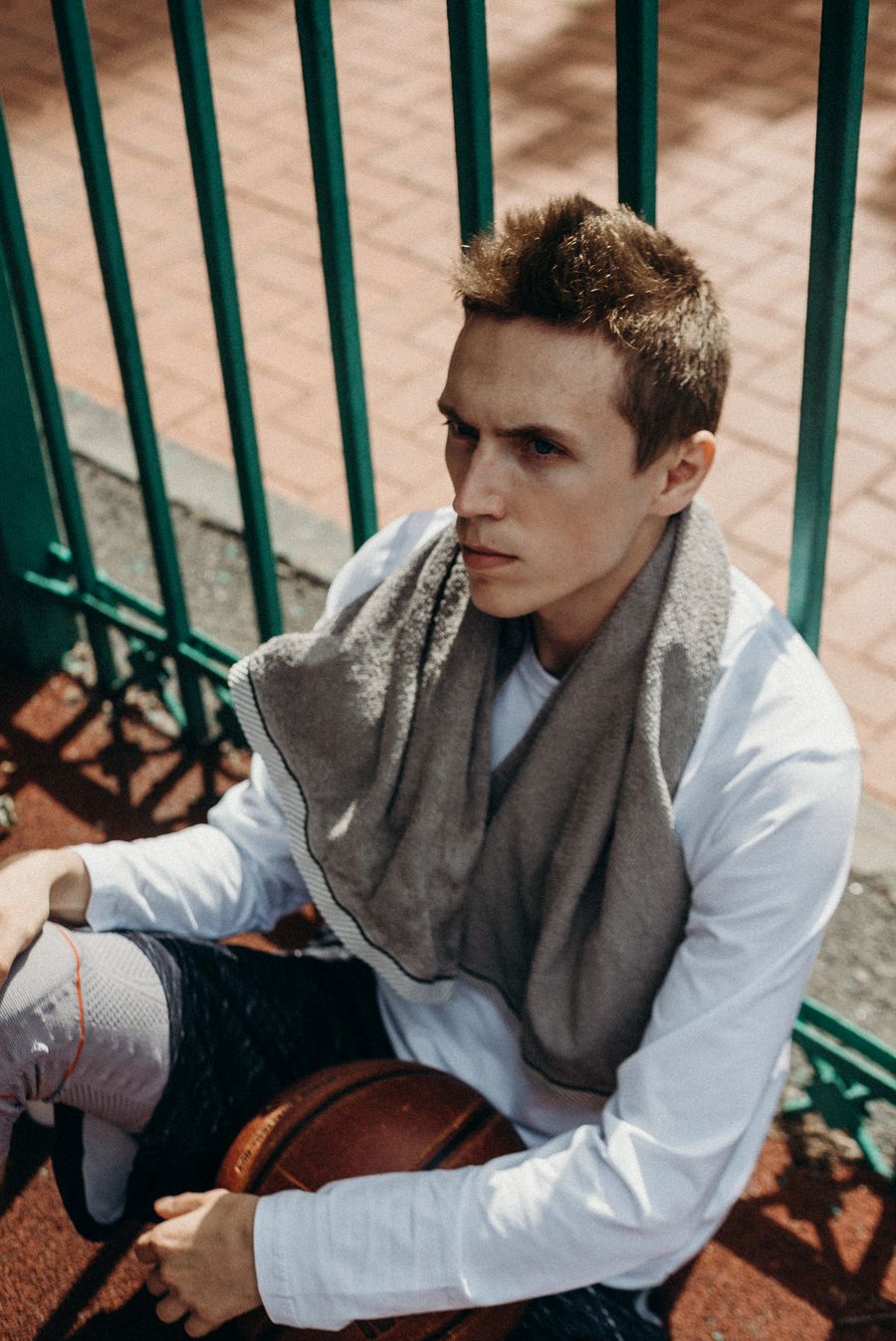 Caucasian male athlete seated outside with a towel, holding a basketball. Outdoor sports setting. Stock Photo