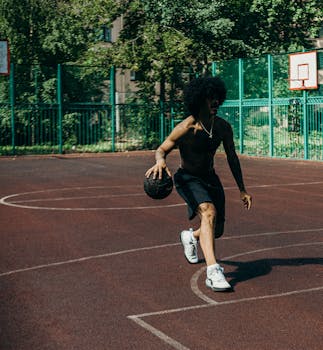 A young man skillfully dribbles a basketball on an outdoor court, showcasing his athleticism and energy.
